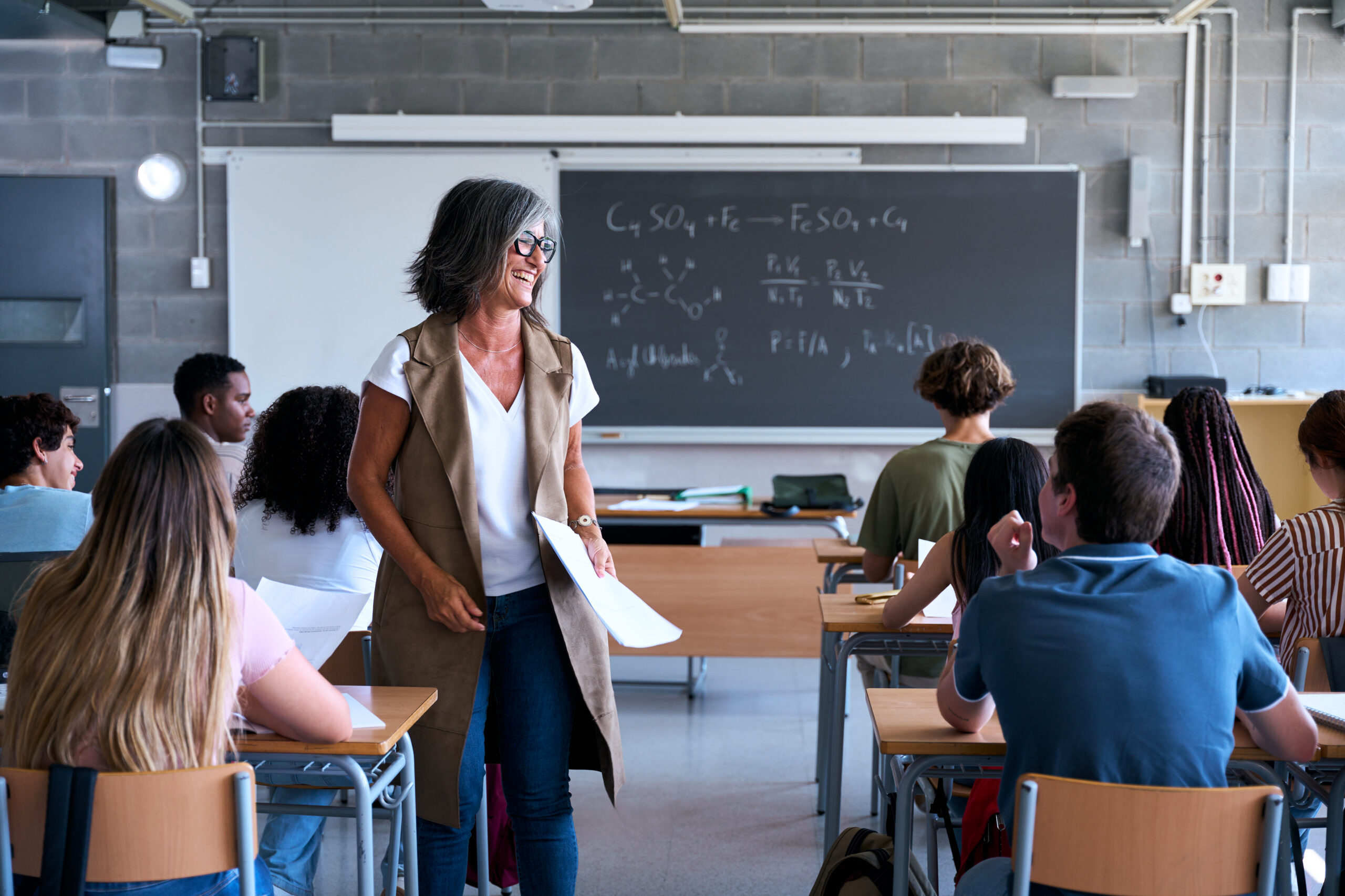 Smiling teacher giving lecture to diverse high school students in classroom