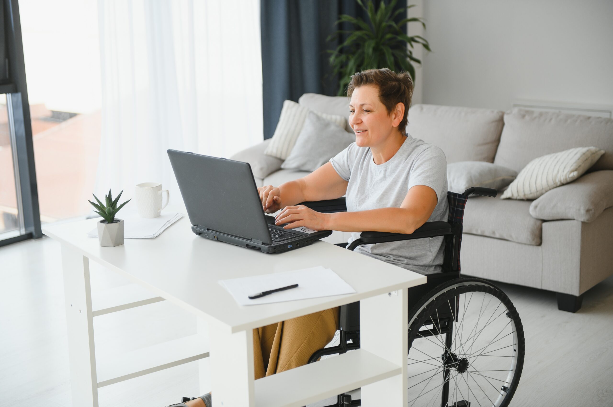 Positive elderly woman in wheelchair working on laptop, IT freelancer, online